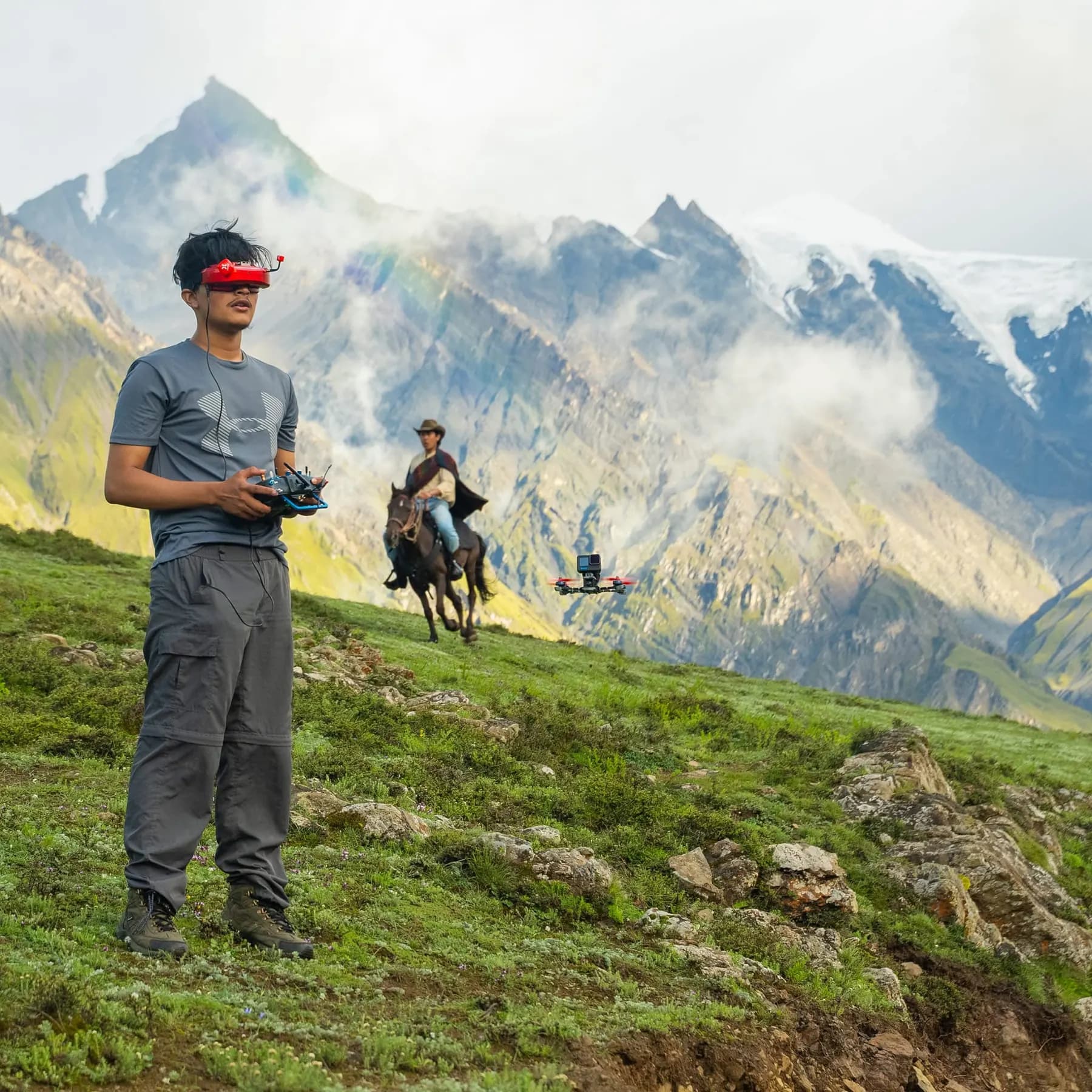 Adarsha Raj Bhusal flying an FPV drone on a mountain slope, goggles on, with a horse rider behind him